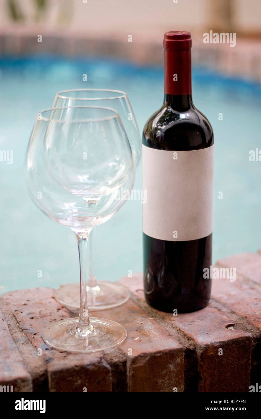 A red wine bottle and two empty glasses by the pool Plenty of copy space on the blank wine label Stock Photo