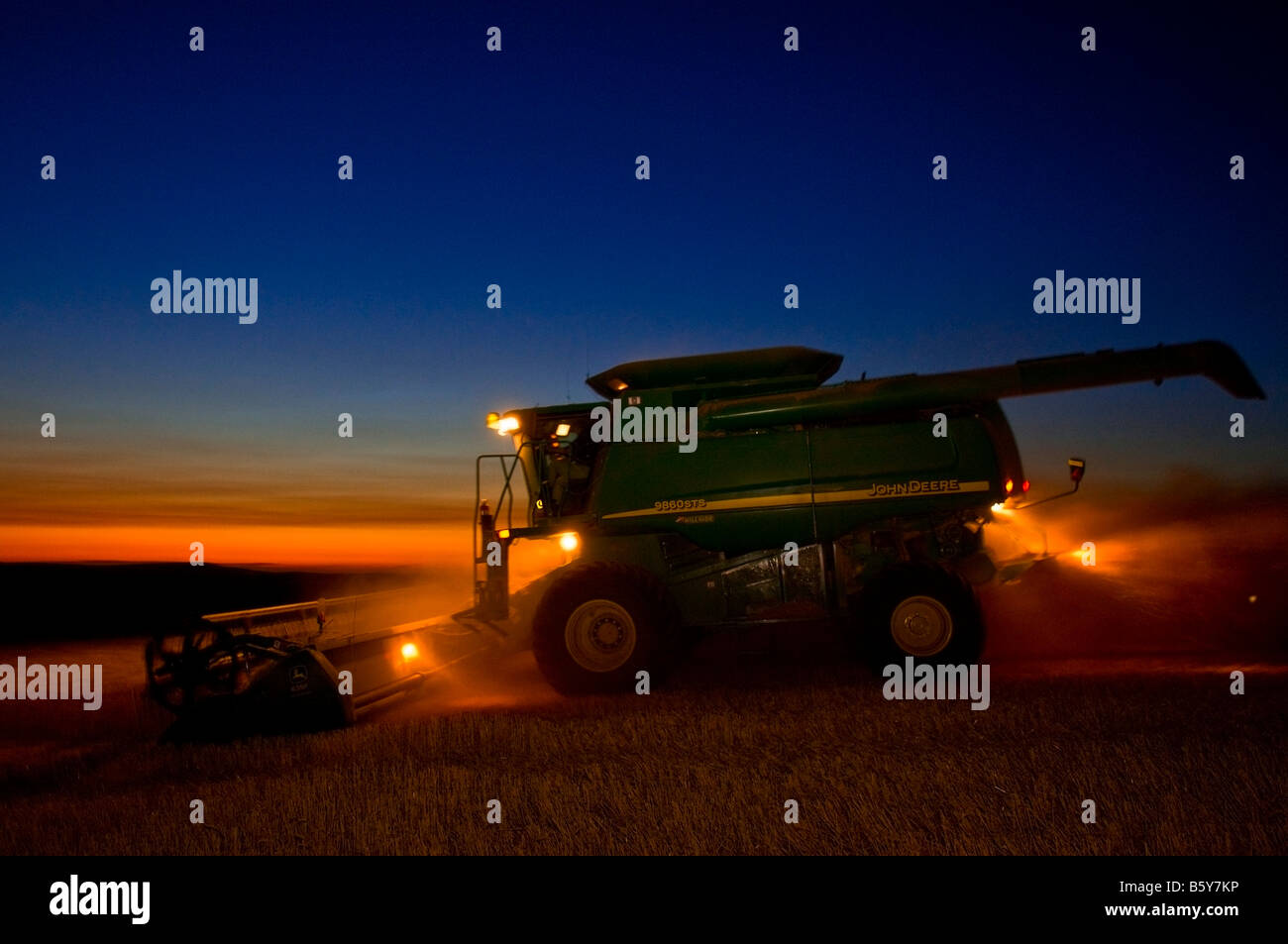 A well lit combine harvests wheat in the evening twilight in the Palouse region of Washington Stock Photo