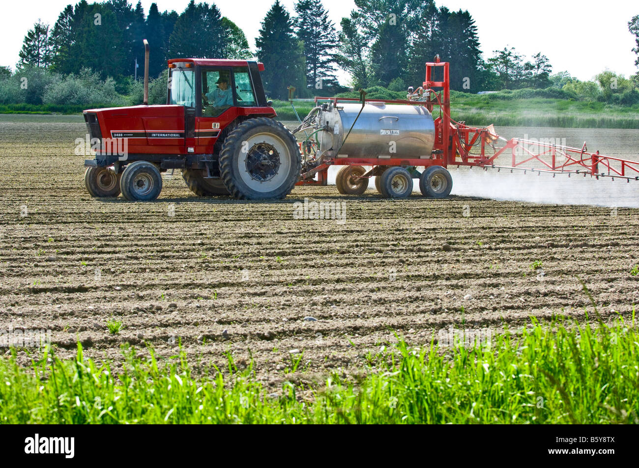 A tractor pulling a spray rig sprays a freshly planted potato field to control weeds in Northwest Washington Stock Photo