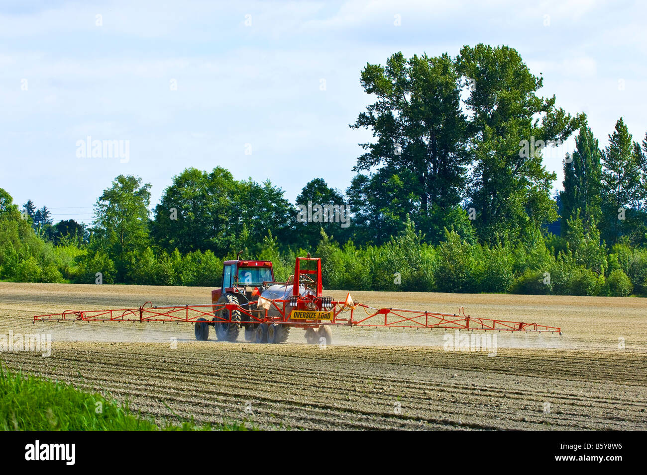 A tractor pulling a spray rig sprays a freshly planted potato field to control weeds in Northwest Washington Stock Photo