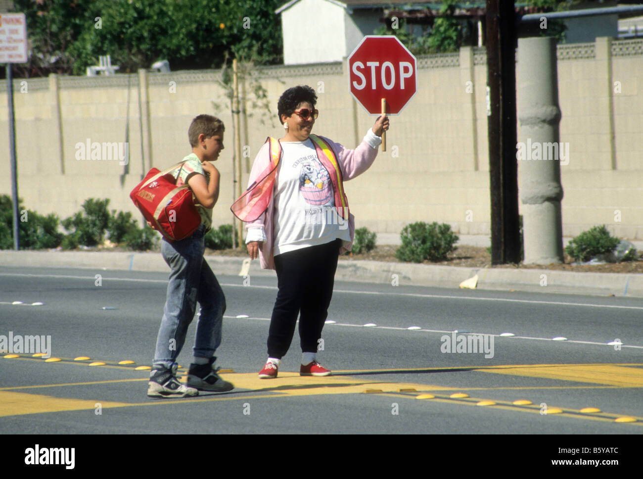 Crossing guard stops traffic so that boy can cross street safely. Stock Photo