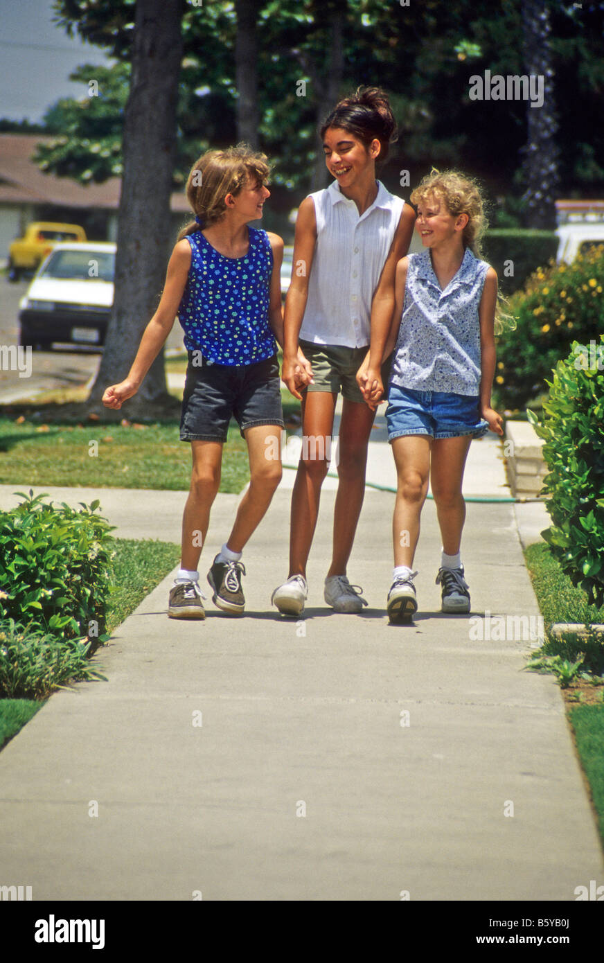 Three young girls walk down the sidewalk during summertime. Stock Photo