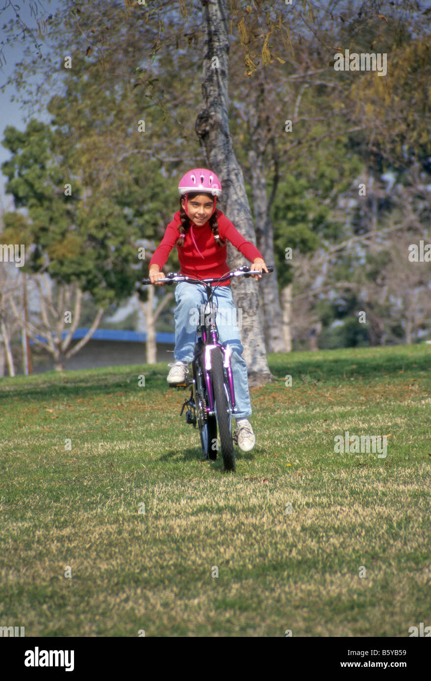 Young girl wearing safety helmet rides bicycle on grass in park Stock Photo