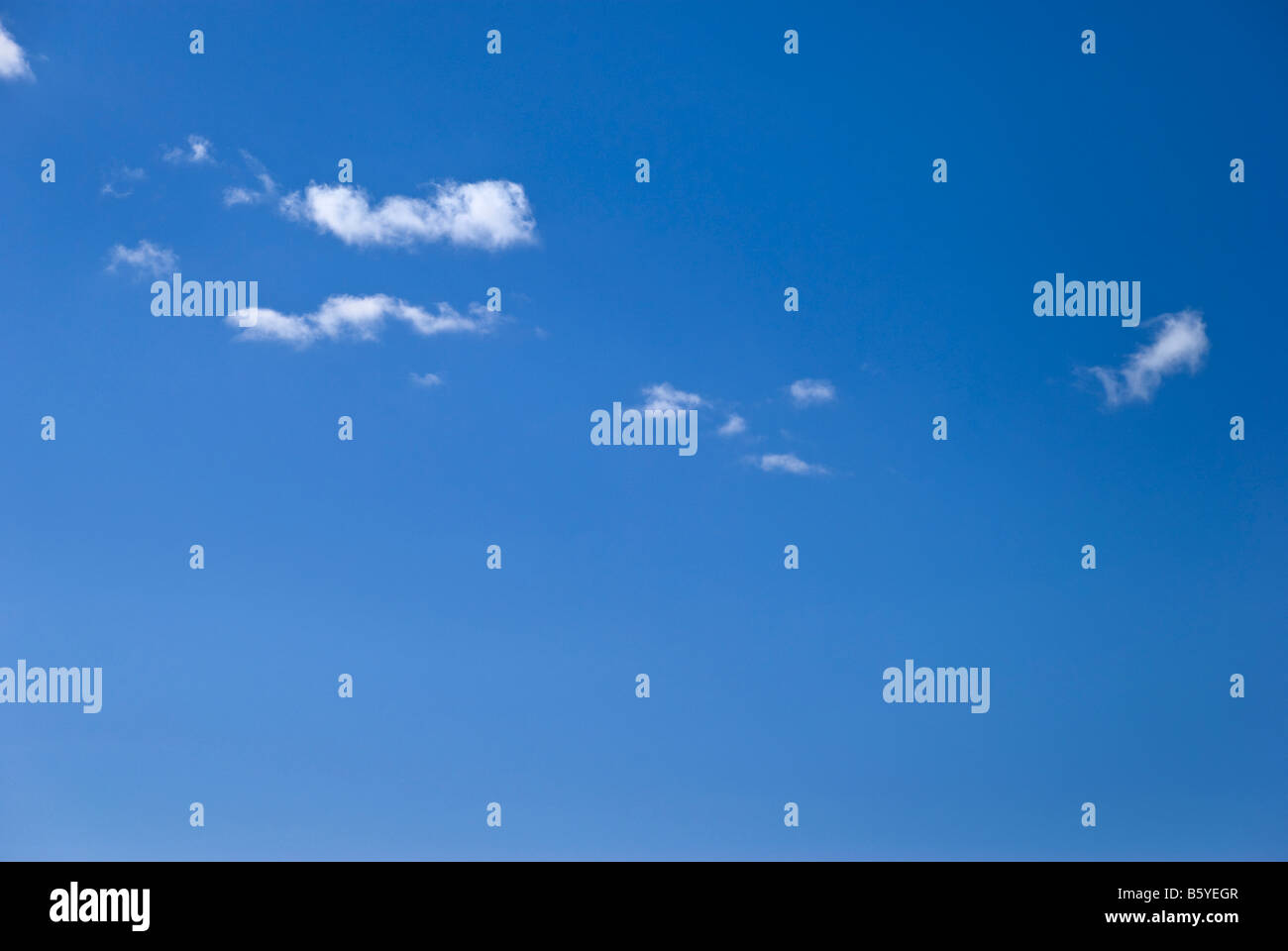 A line of fluffy or cotton wool like clouds float against a perfect clear blue sky Stock Photo