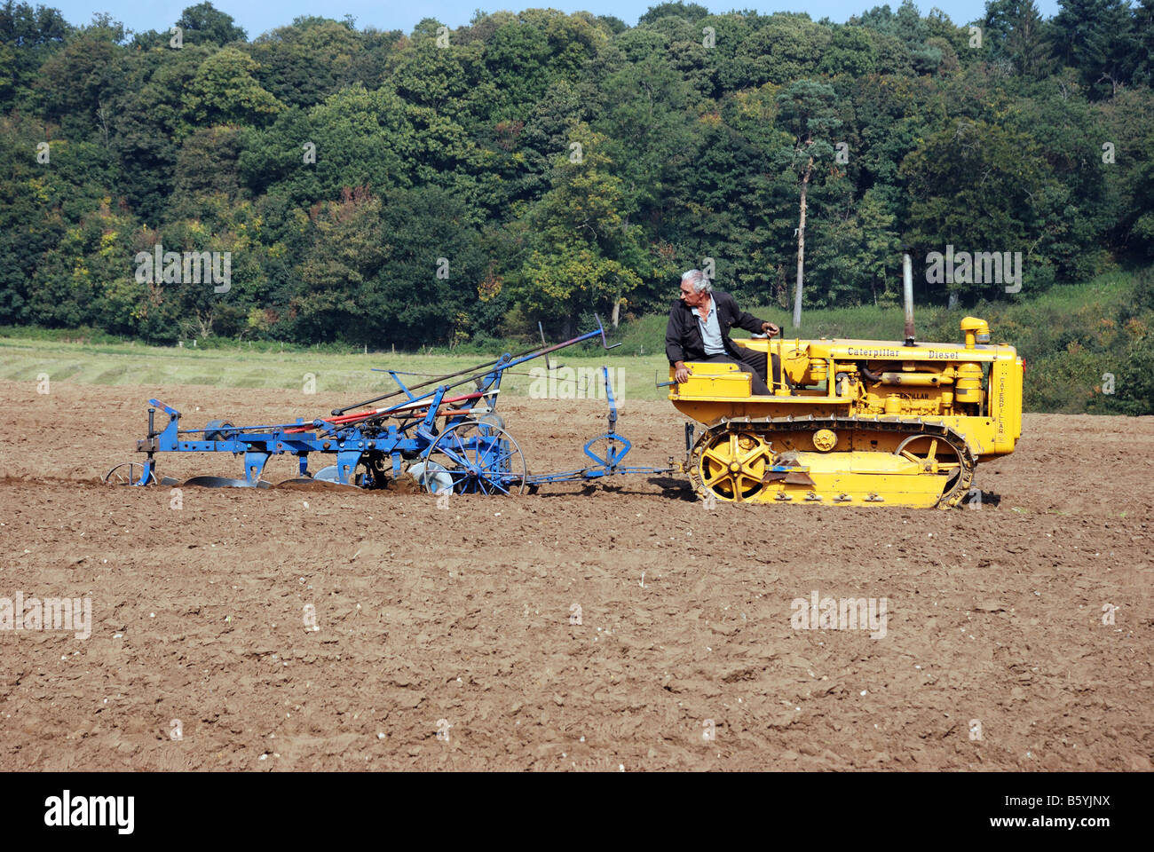 Yellow Caterpillar diesel tracked tractor pulling a blue plough at the