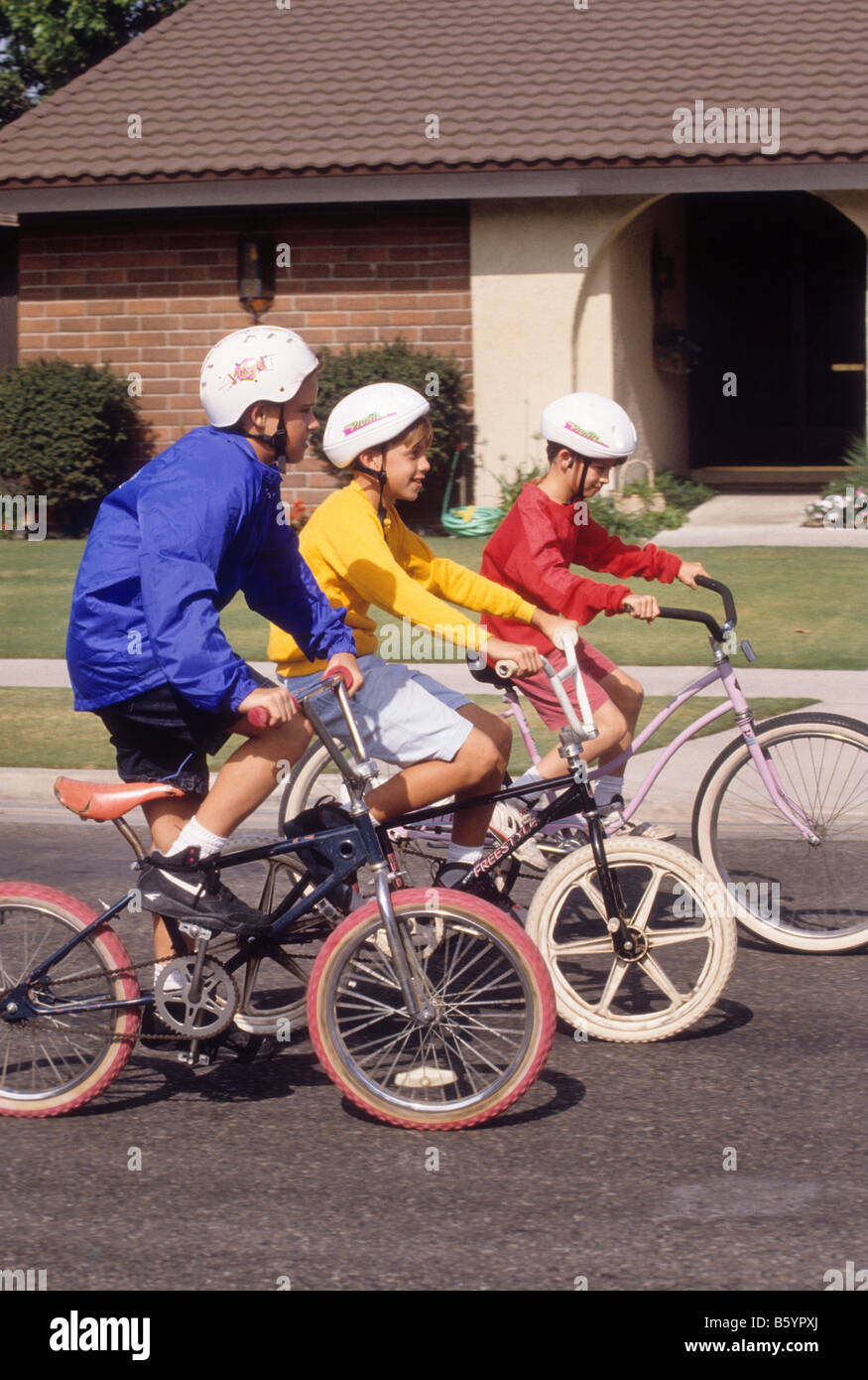 Three boys wearing safety helmets ride bikes in street Stock Photo