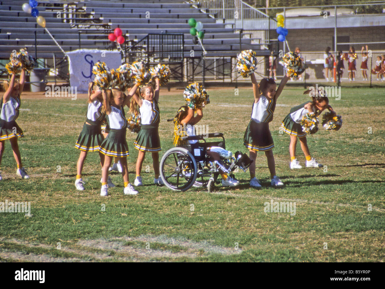 Squad of little girls, one in wheelchair, cheers during competition at football game, USA Stock Photo