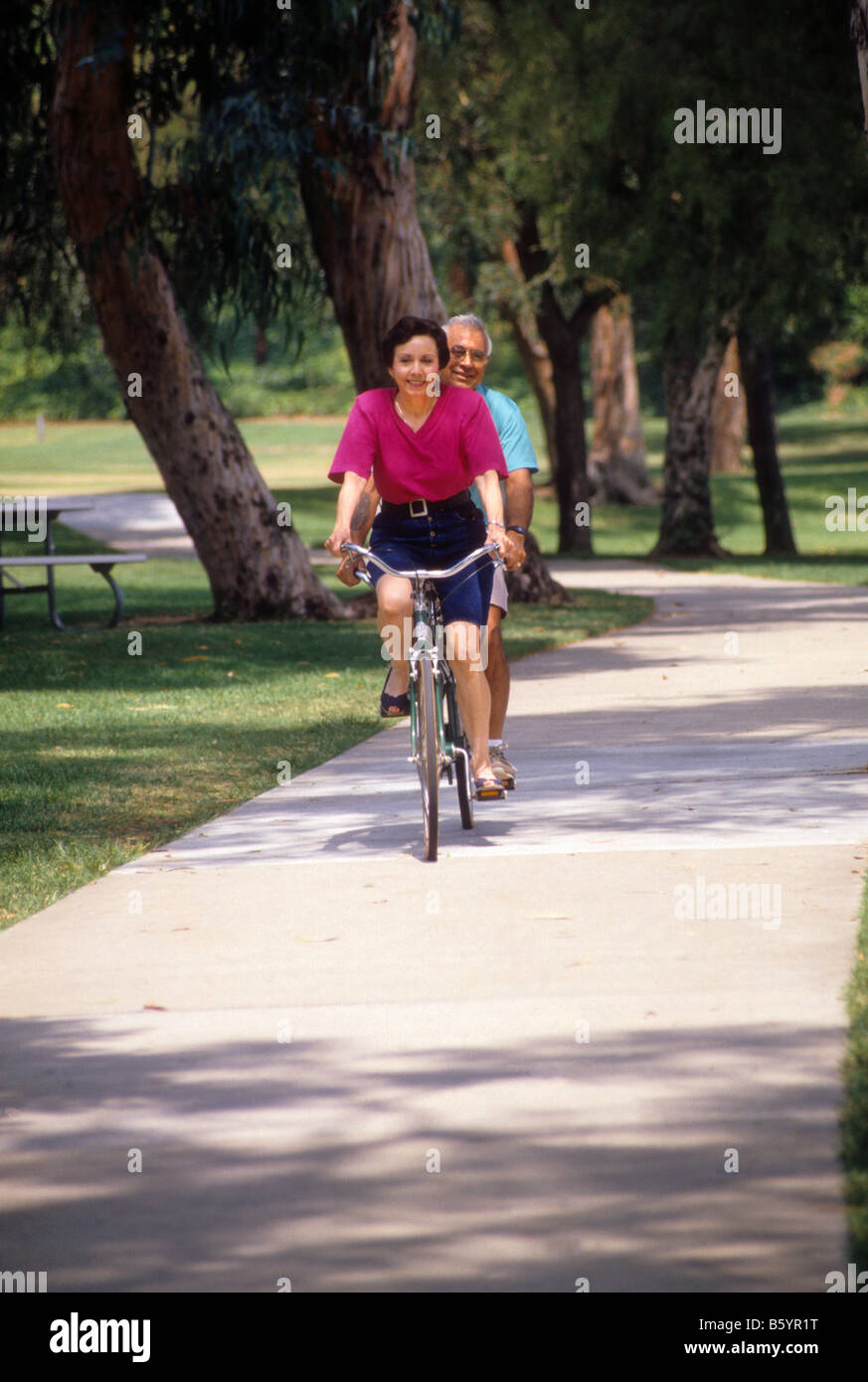 Hispanic couple ride tandem bicycle in park. Stock Photo