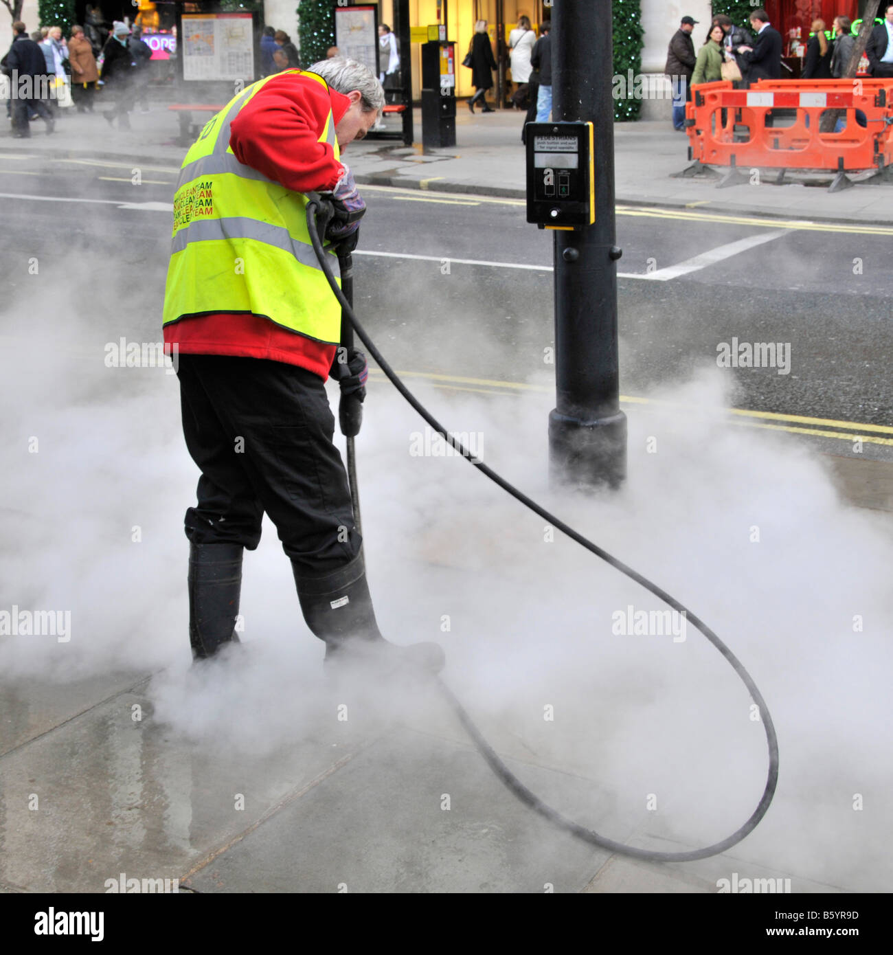 Council workman wearing high visibility vest isteam cleaning sticky chewing gum mess from pavements in Oxford Street West End London England UK Stock Photo