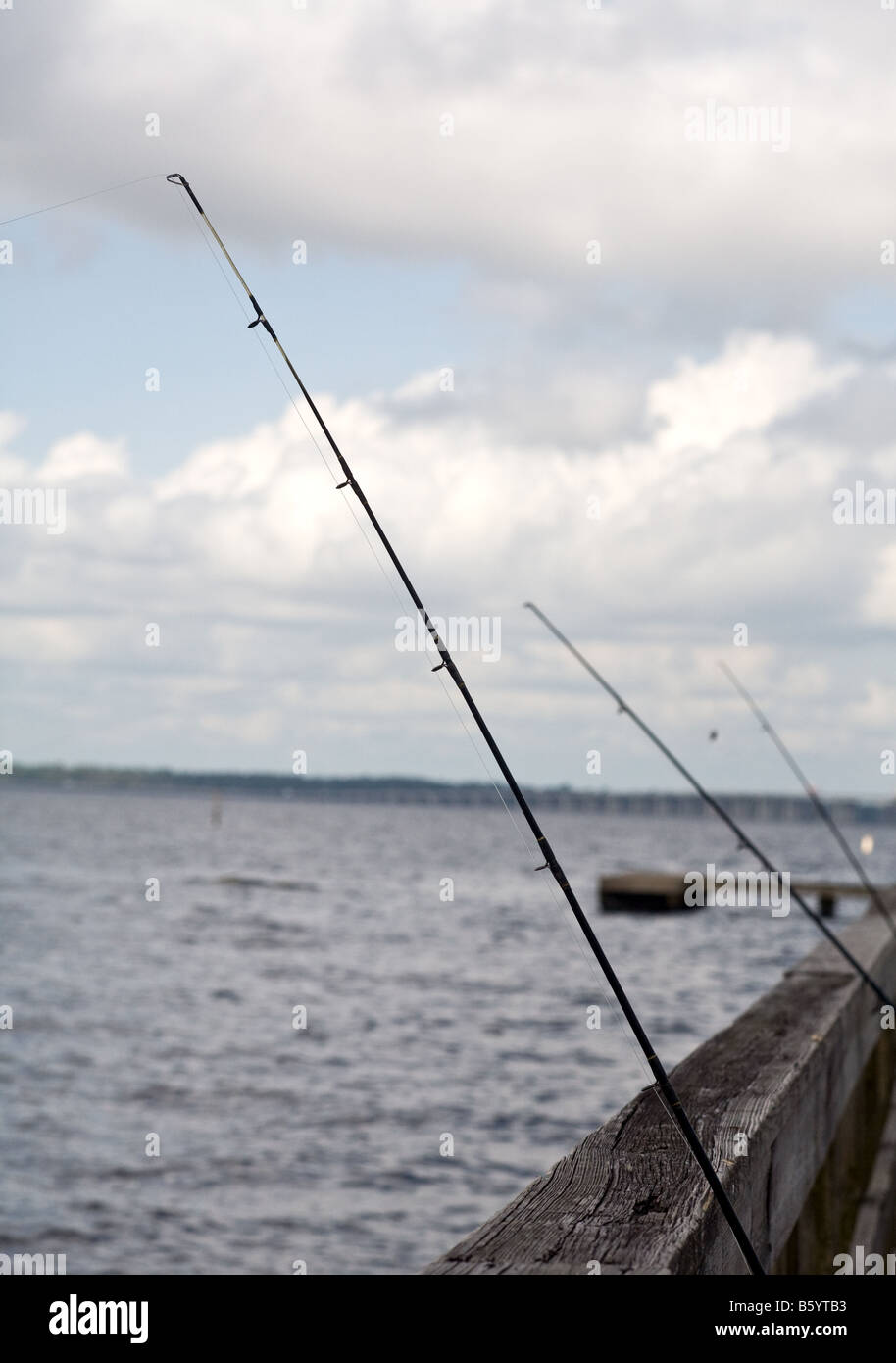 A fishings pole leaning against the wooden railing by the water Stock Photo  - Alamy