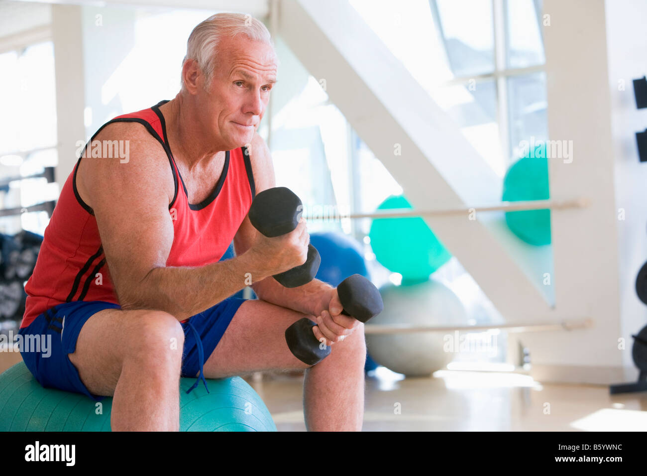 Man Using Hand Weights On Swiss Ball At Gym Stock Photo Alamy