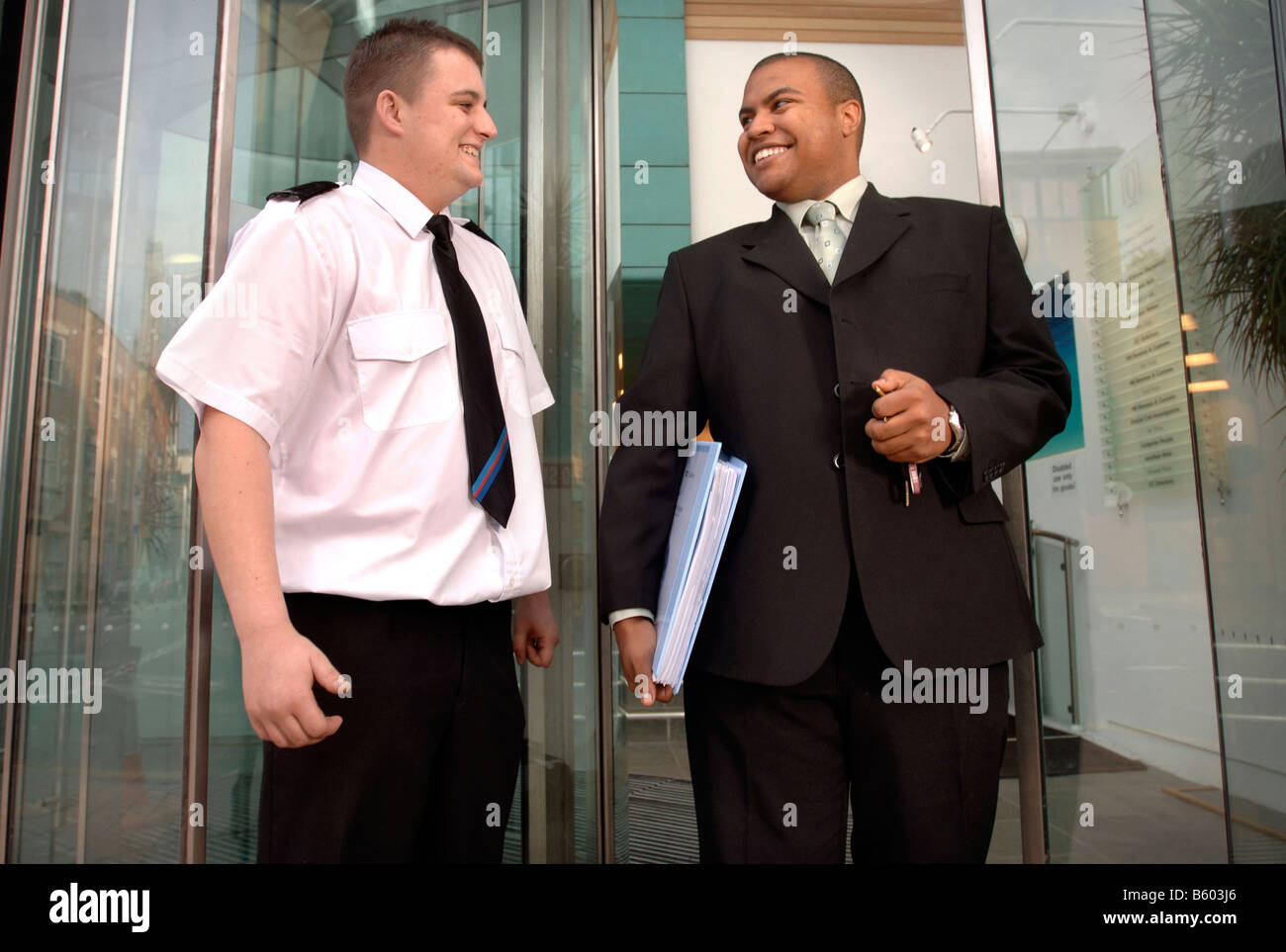 A SECURITY GUARD ON PATROL UNLOCKS THE DOOR OF A BUSINESS PREMISES TO ALLOW A LATE WORKING EMPLOYEE TO LEAVE UK Stock Photo