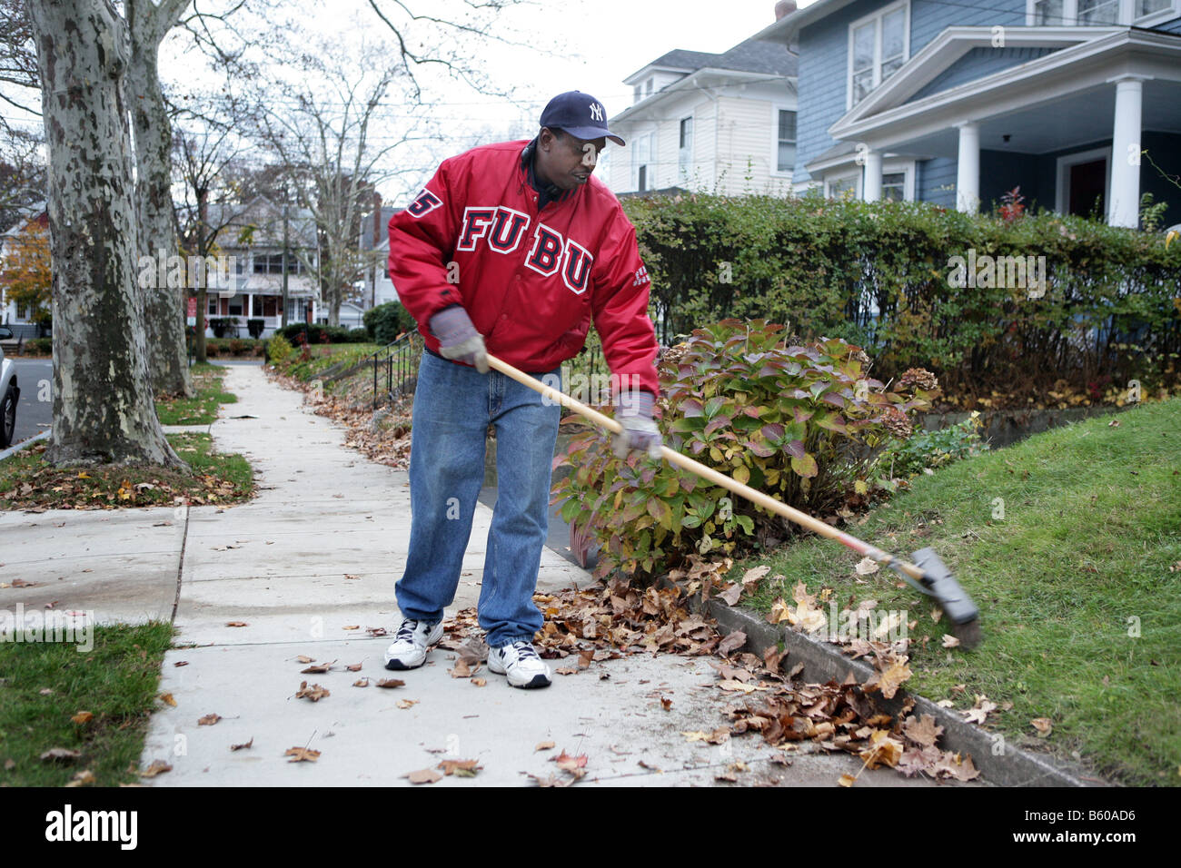 A man sweeps leaves in front of his home in New Haven Connecticut USA Stock Photo