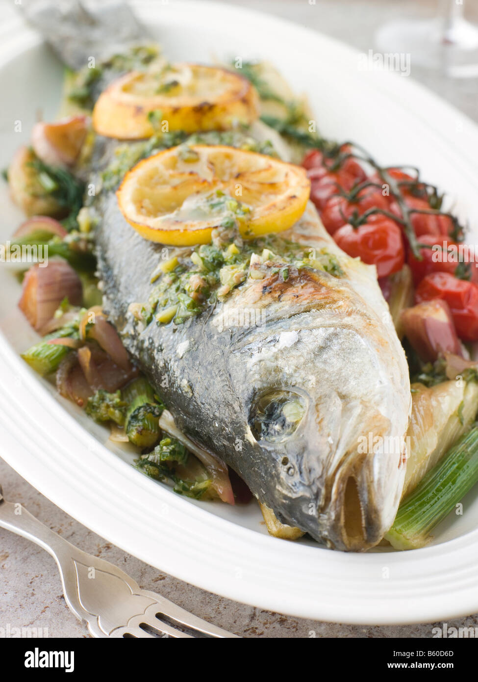 Whole Roasted Sea Bass with Fennel Lemon Cherry Vine Tomatoes and Salsa Verde Stock Photo
