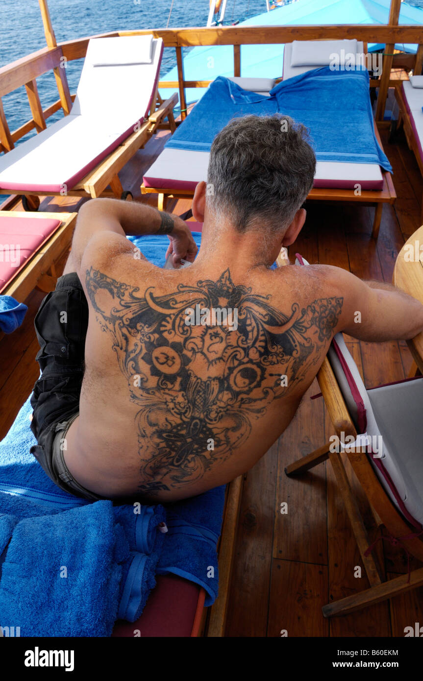 Heavily tattooed man relaxing on the sun deck of the MS-Felicia, Komodo National Park, World Heritage Site, Komodo, Indonesia Stock Photo