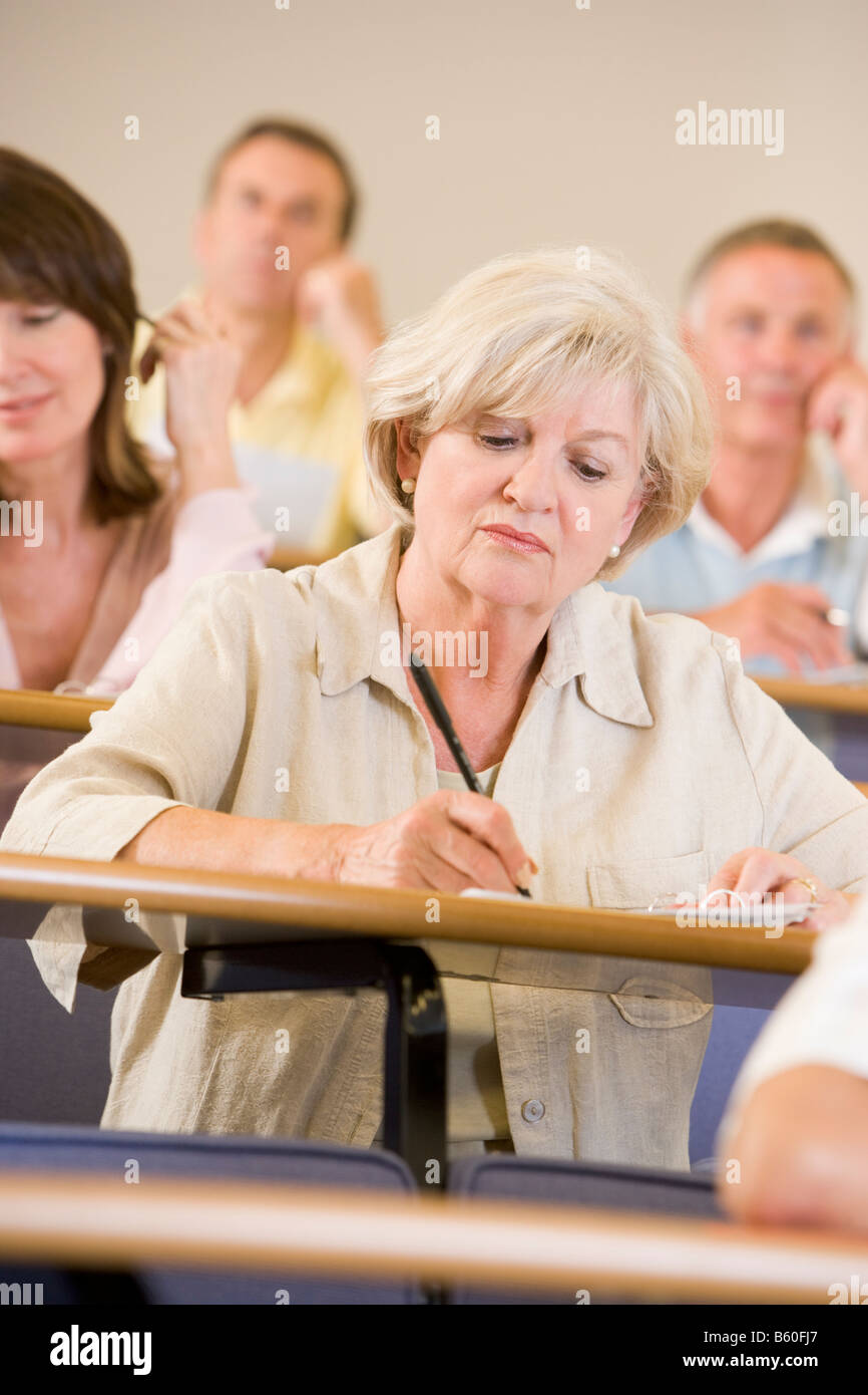 Woman sitting in adult classroom taking notes with students in background (selective focus) Stock Photo