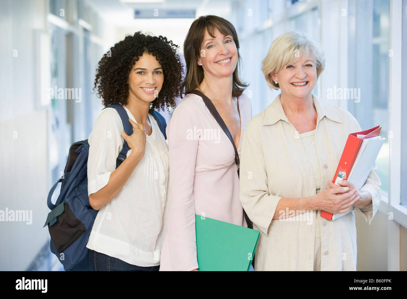 Three women standing in corridor with books (high key) Stock Photo