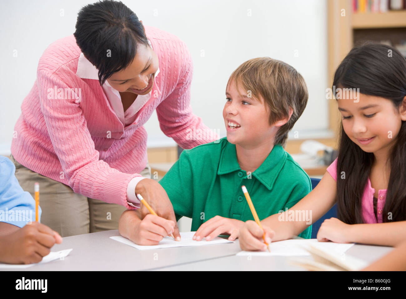 Students in class writing with teacher helping Stock Photo Alamy