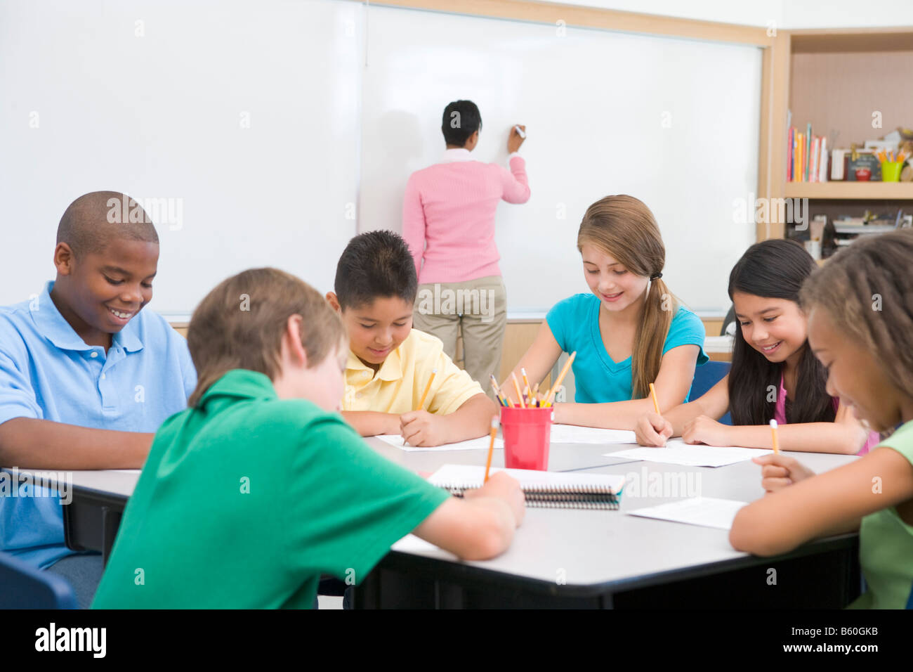 Students in class writing with teacher at front board Stock Photo