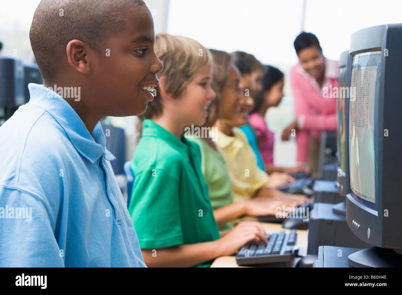 Six children at computer terminals with teacher in background (depth of ...