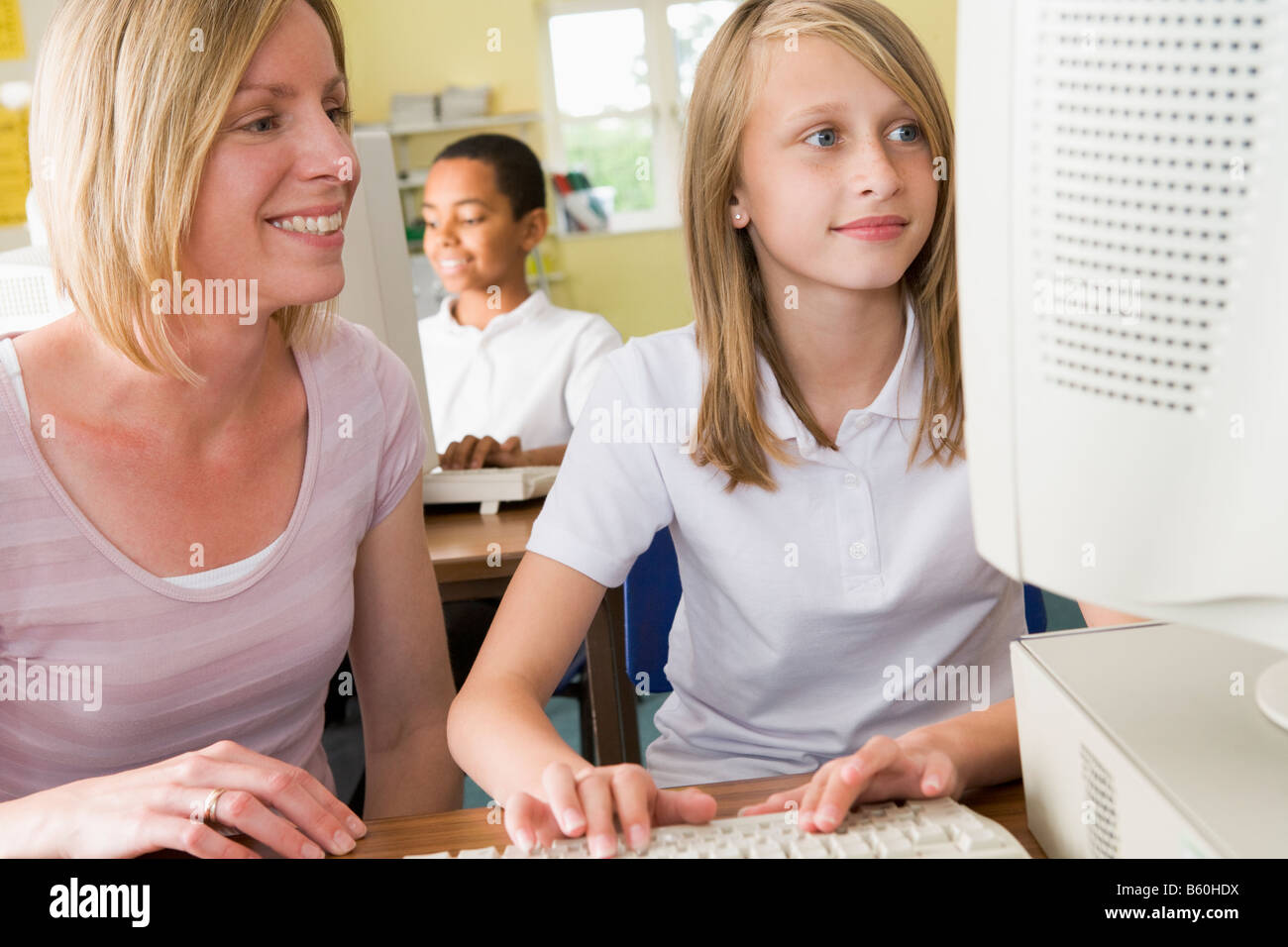 Student and teacher at computer terminal typing with student in background (selective focus) Stock Photo