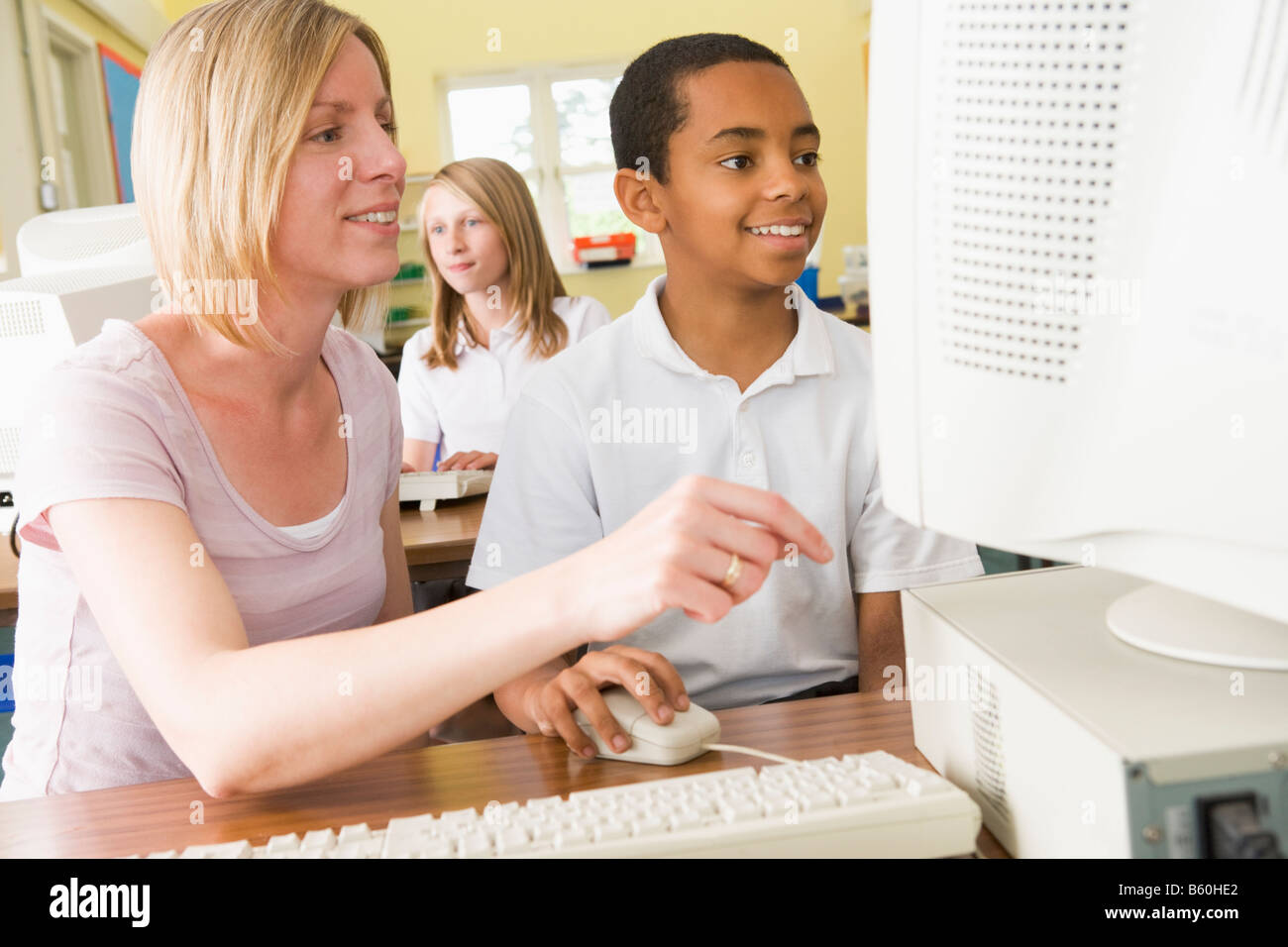 Student and teacher at computer terminal with student in background Stock Photo