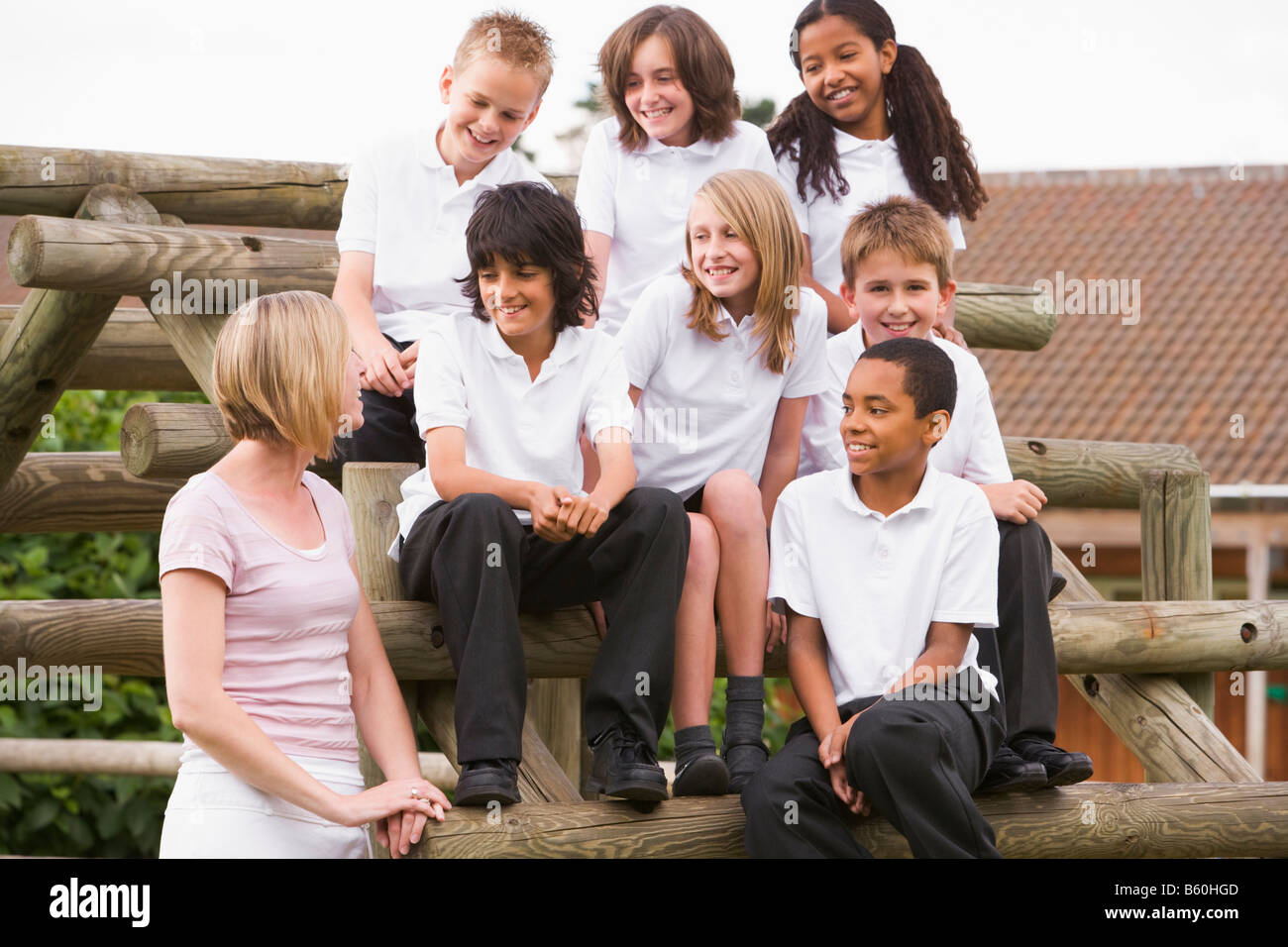 Seven students sitting on wooden structure with teacher standing beside them Stock Photo