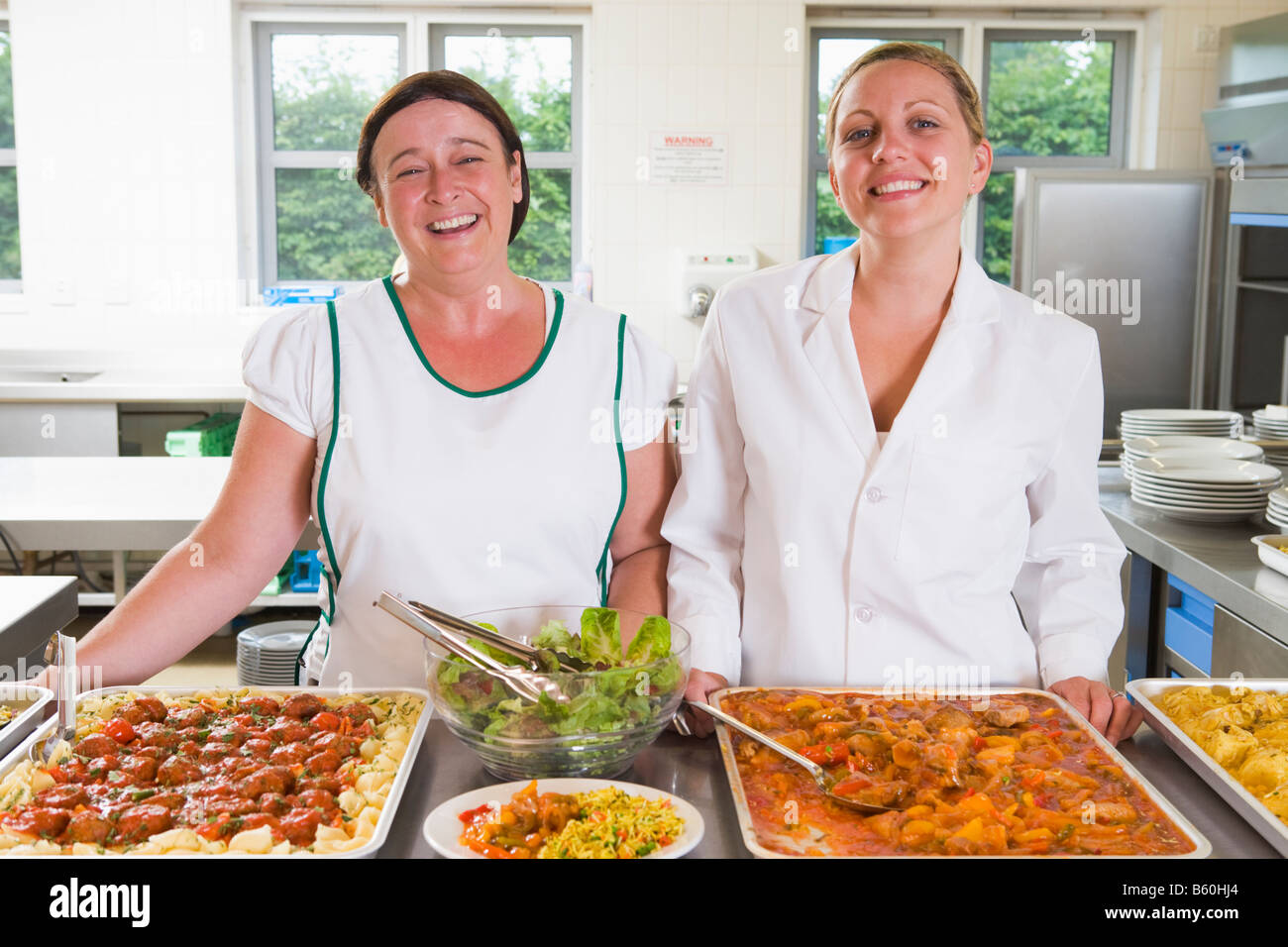 Two lunch ladies standing behind full lunch service station Stock Photo