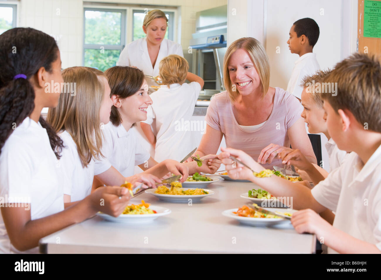 Students sitting at cafeteria table eating lunch with teacher Stock Photo