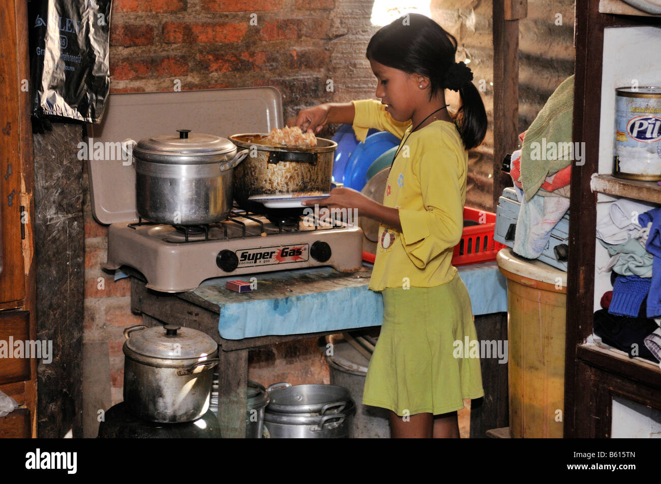 Girl filling her plate in a poor kitchen, Slum Area Plan 3000, Santa Cruz, Bolivia, South America Stock Photo