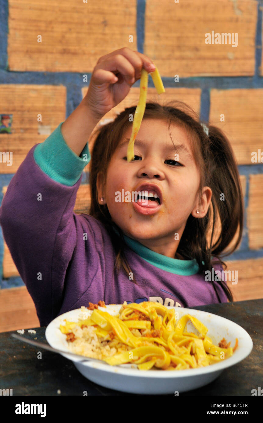 Girl eating ribbon noodles with her fingers, Slum Area Plan 3000, Santa Cruz, Bolivia, South America Stock Photo