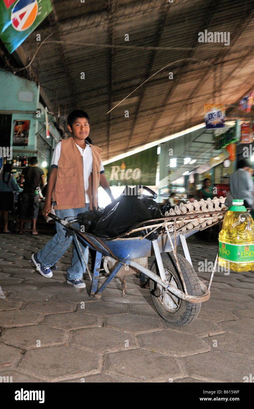 Child labour, boy transporting customers' purchases using a wheel barrow at the local market, Santa Cruz, Bolivia, South America Stock Photo