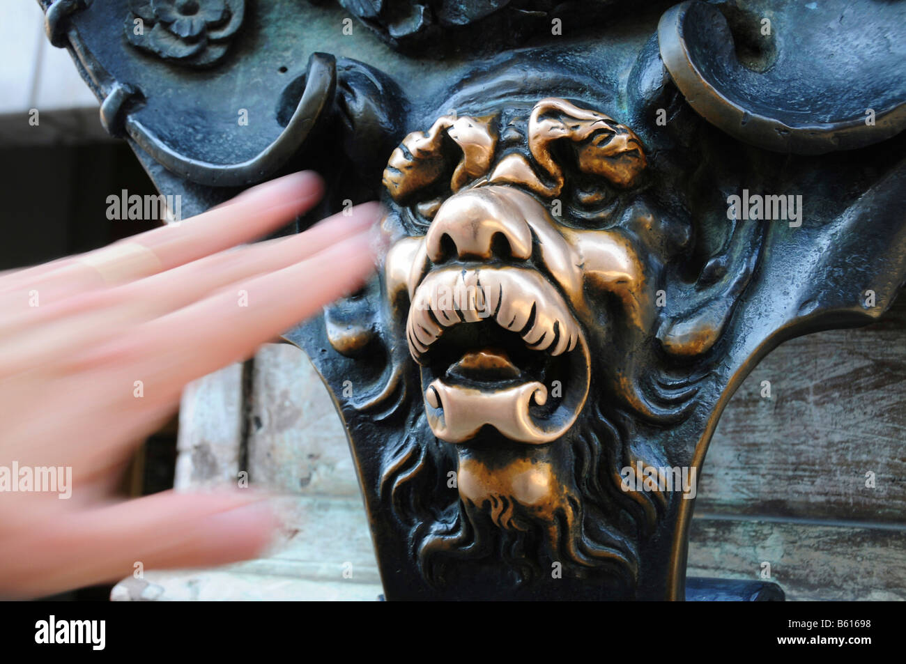 Hand reaching to touch the bronze head of a lion for the fulfilment of a wish, on the Residenz building in Munich, Bavaria Stock Photo
