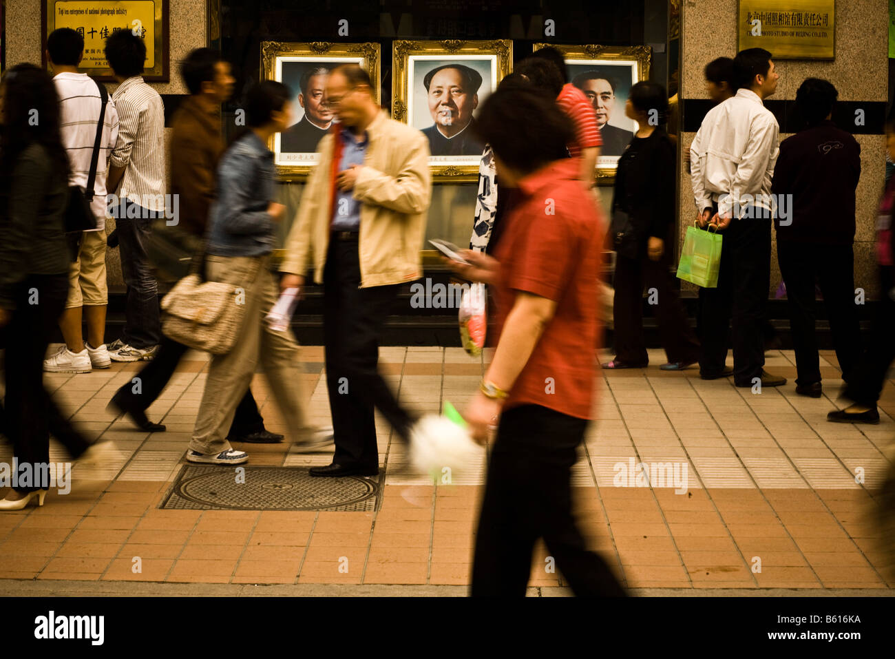 People walk by a portrait of Chairman Mao Zedong in a busy shopping area in Beijing China in April 2008 Stock Photo