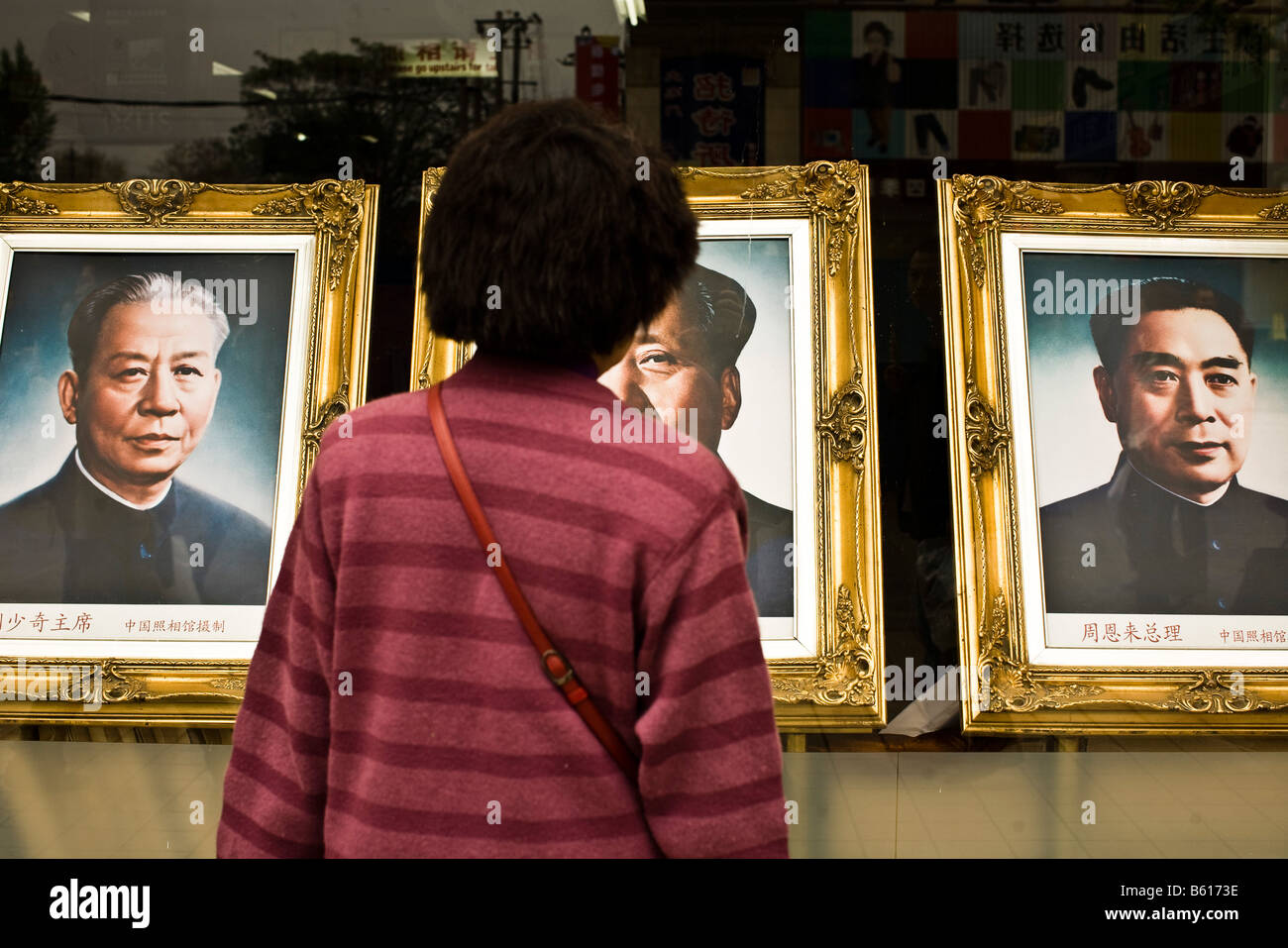 A woman looks at photos of Zhou Enlai Mao Zedongat a busy shopping center in Beijing China in April 2008. Stock Photo
