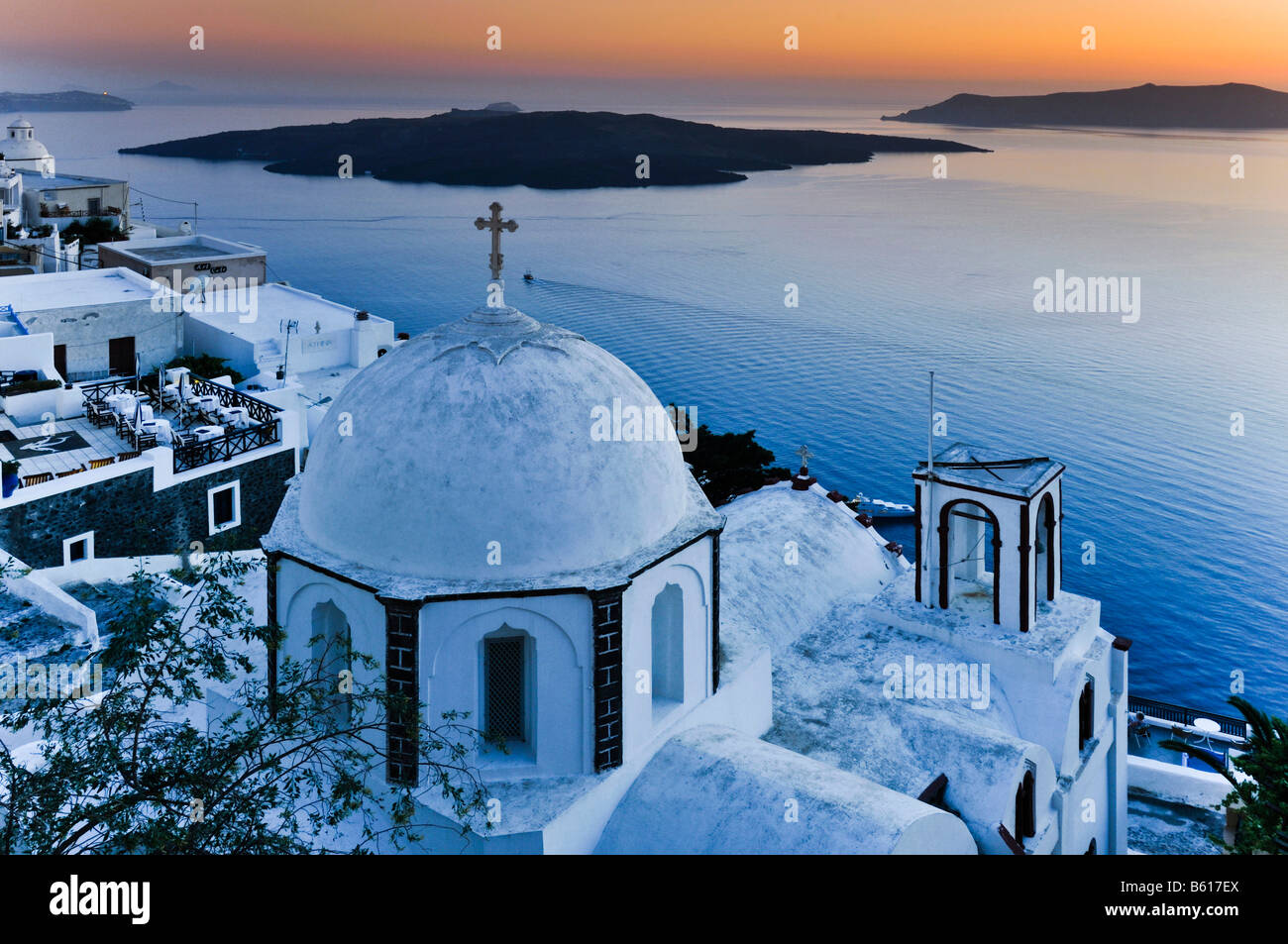 White domed church with a cross at sunset in front of the sea and the volcanic island of Nea Kameni, Santorini, Cyclades, Greece Stock Photo