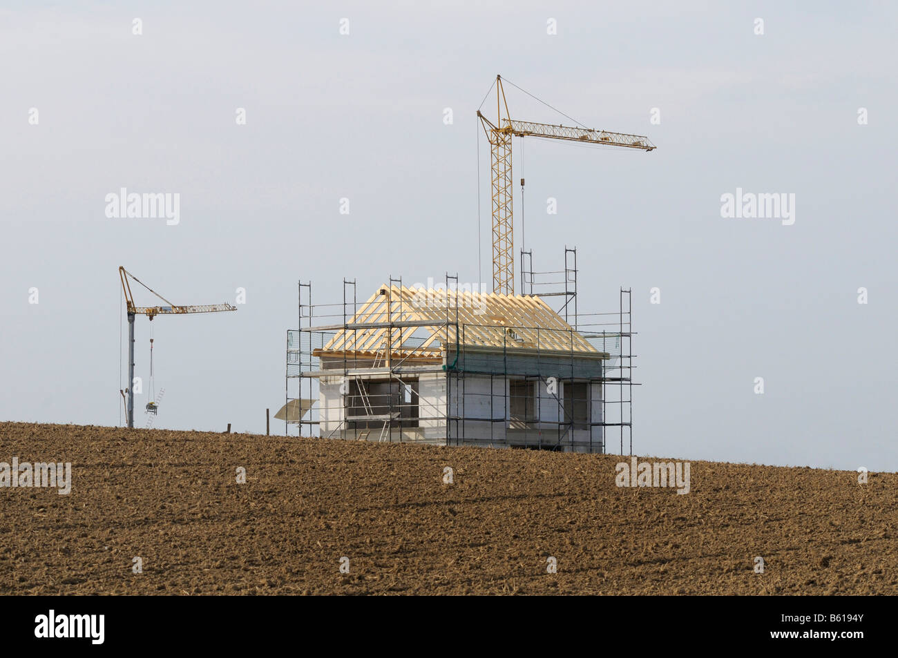 Scaffolded building shell with roof truss in an empty field, flanked by ...