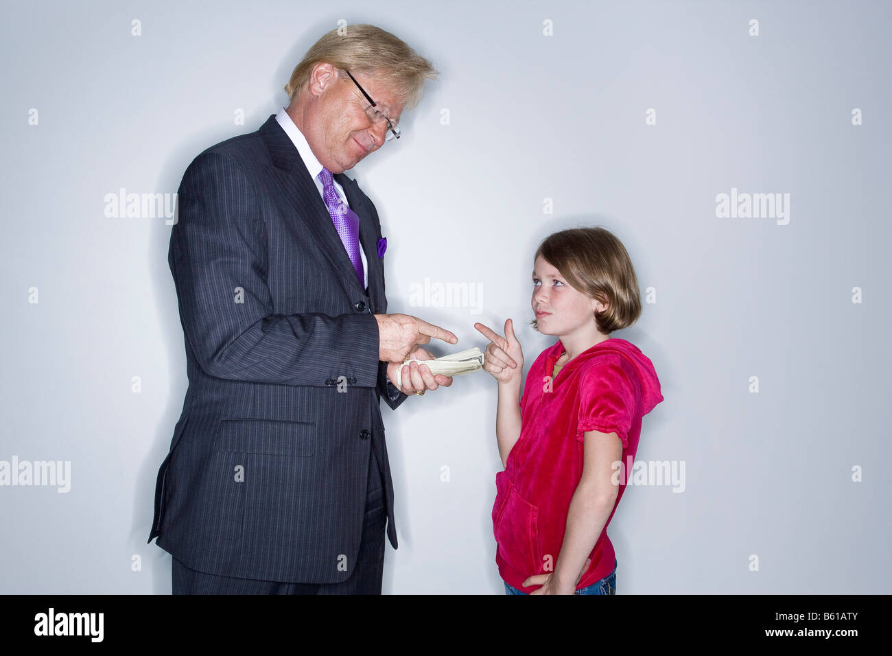 Business man in a suit and tie about to give cash money to a  9 year old girl in a bright pink shirt. Stock Photo