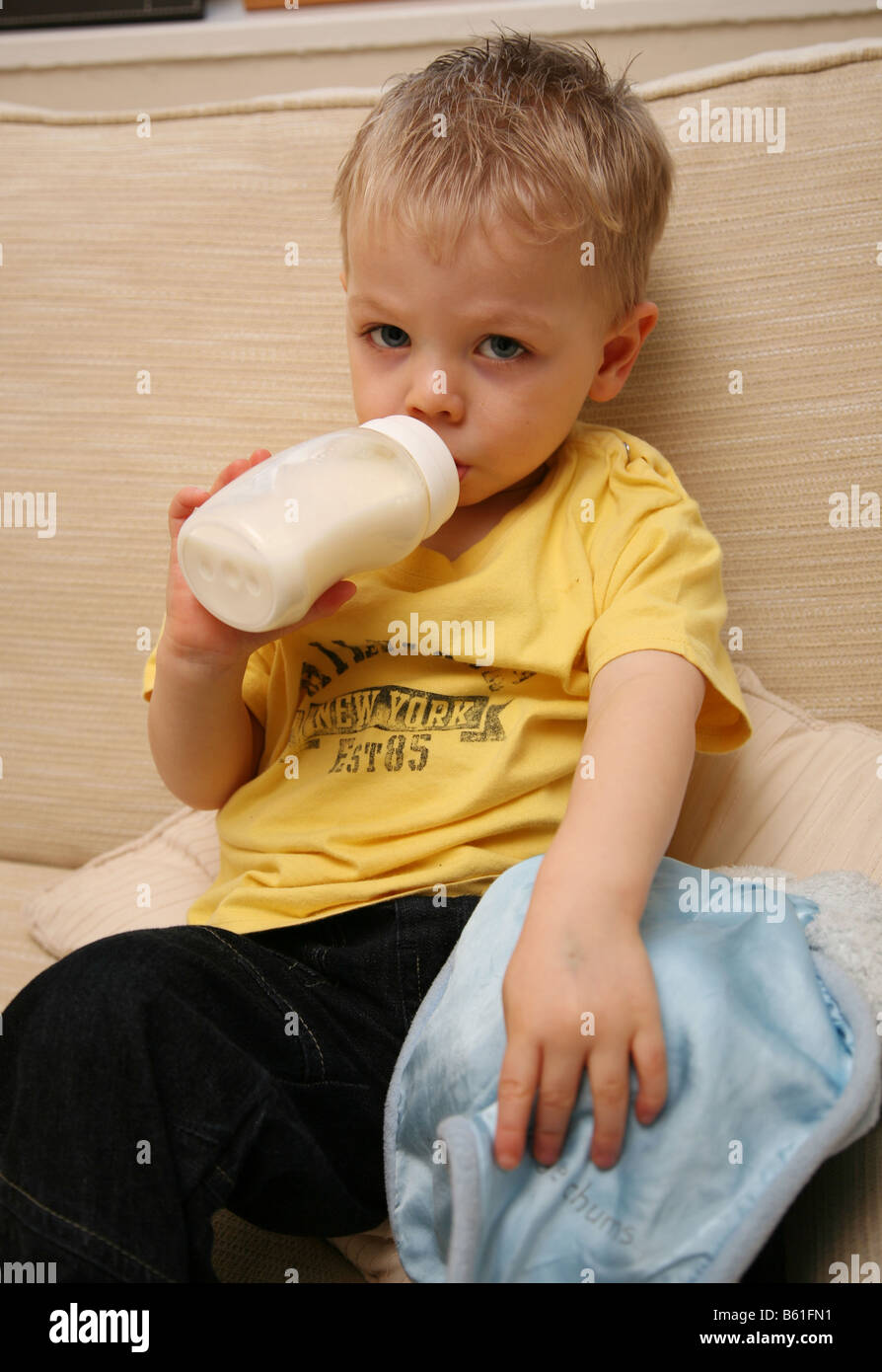 Tired 2 year old boy drinking warm milk from the bottle and holding his comfort blanket Stock Photo