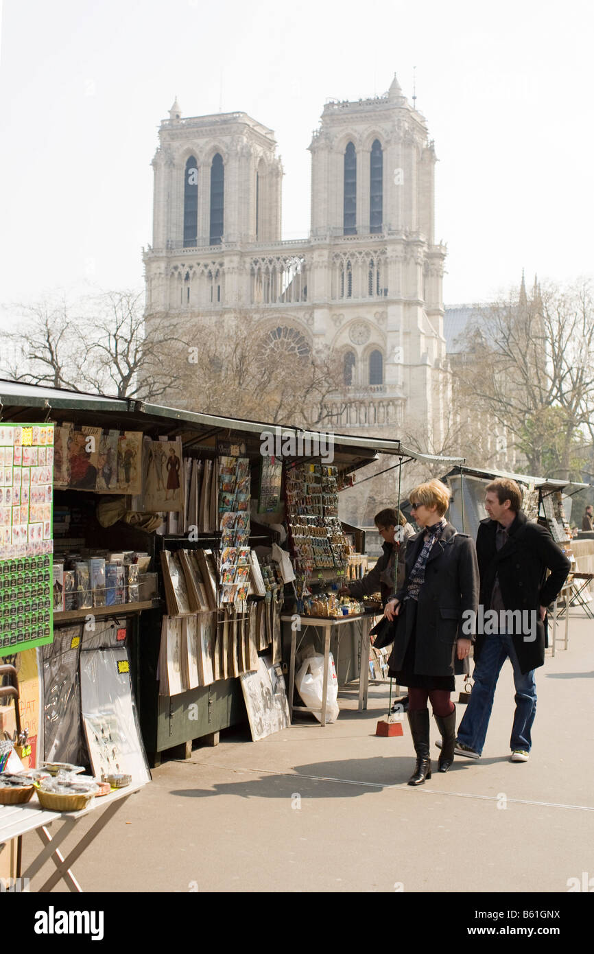 Observers pass art stands and vendors on the Left Bank of Paris’ Seine River, with the Cathedral of Notre-Dame in the background Stock Photo