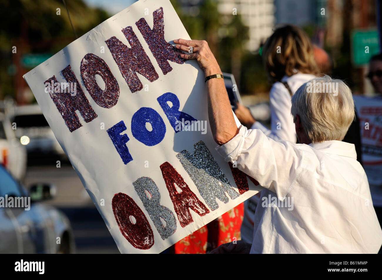 Female senior citizen shows sign for Barack Obama for President on busy road Stock Photo