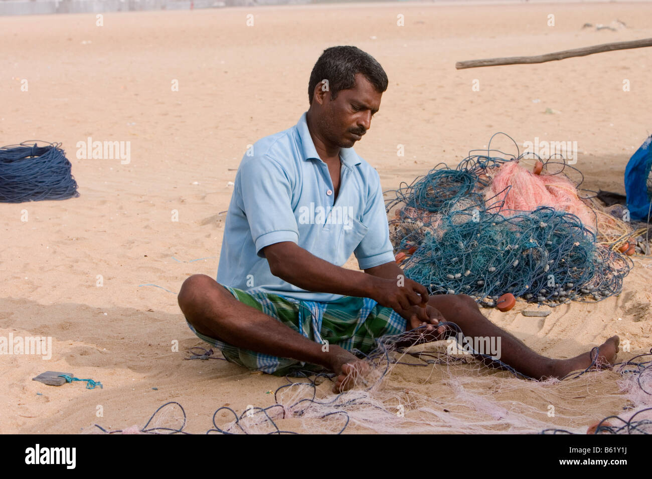 Fisherman mending his nets at the Marina Beach, Chennai Stock