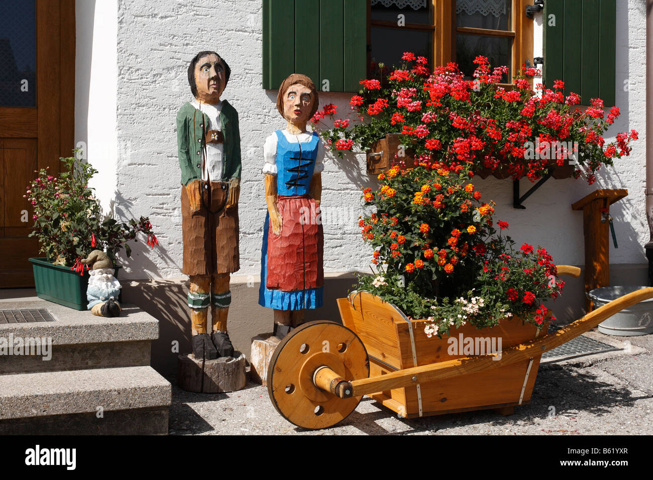 Wooden figures of a couple, wooden barrow in front of a farmhouse in Stoetten am Auerberg, interior view, Allgaeu, Swabia, Bava Stock Photo