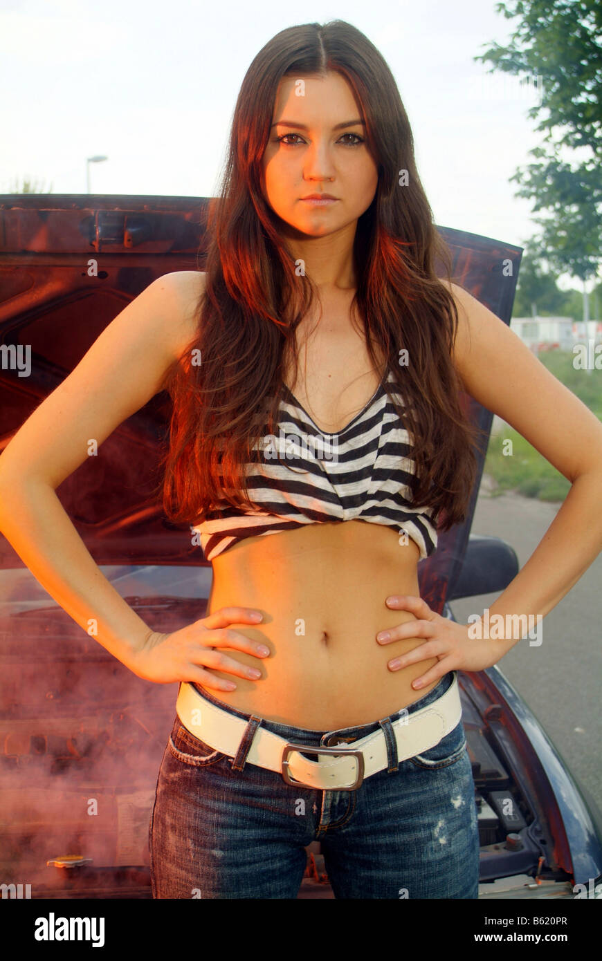 Young woman standing in front of her smoking car, looking mad Stock Photo