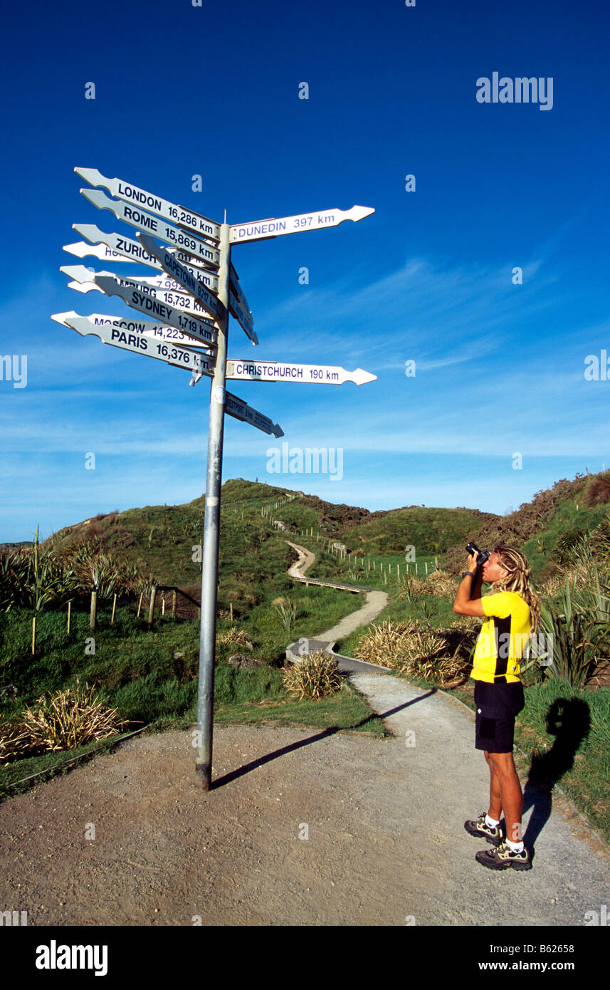 Tourist taking a photo of a direction signpost, Punakaiki, Pancake Rocks, South Island, New Zealand Stock Photo