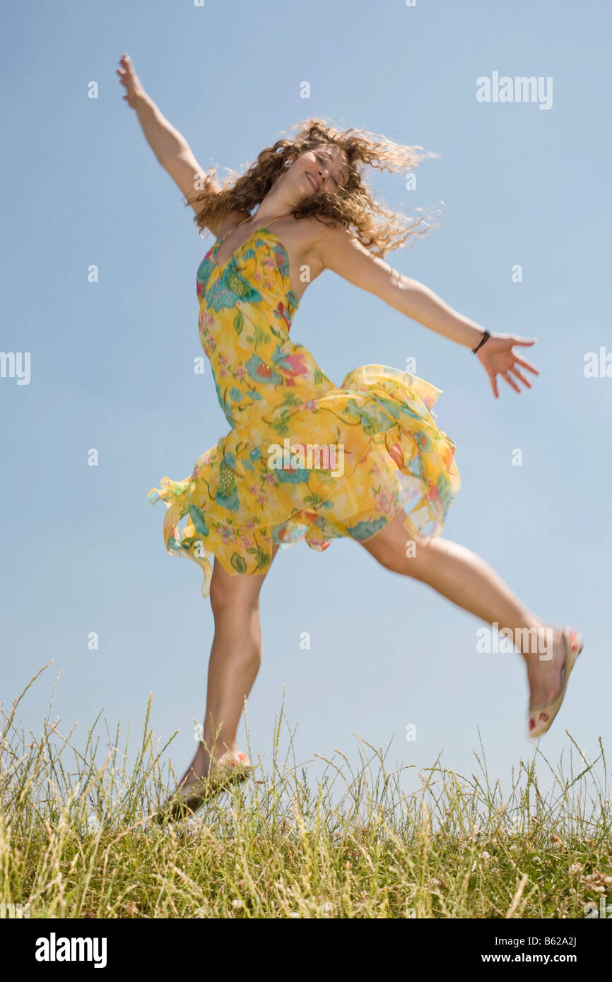 Young woman with long hair wearing a yellow dress jumping in front of a ...