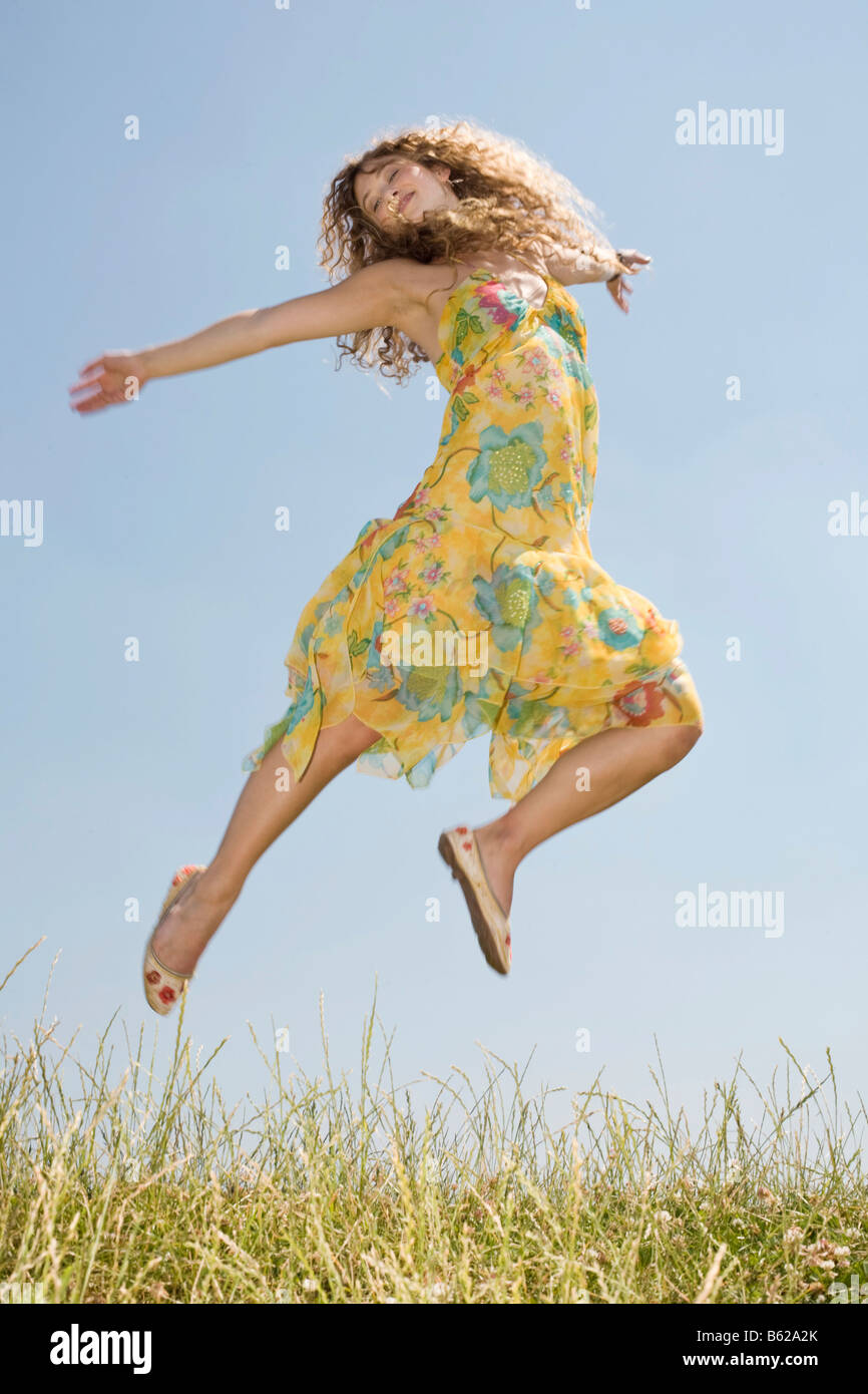 Young woman with long hair wearing a yellow dress jumping in front of a ...