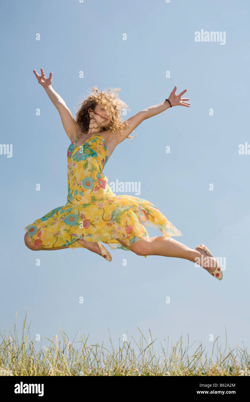 Young woman with long hair wearing a yellow dress jumping in front of a ...