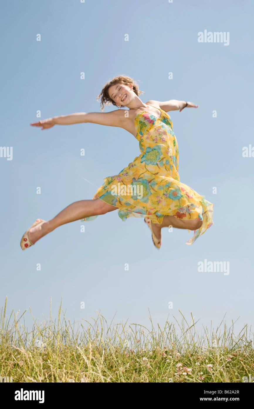 Young woman with long hair wearing a yellow dress jumping in front of a ...