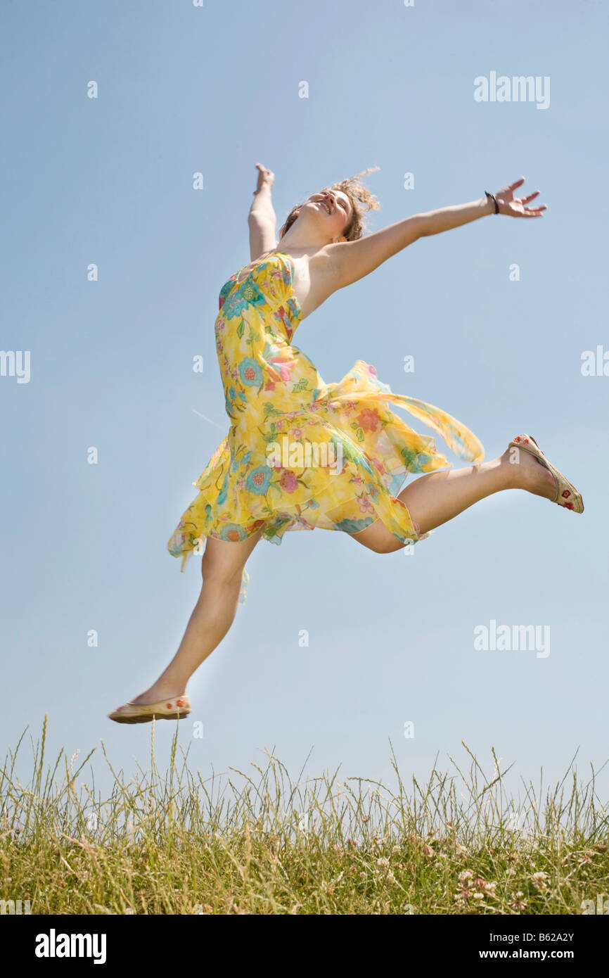 Young woman with long hair wearing a yellow dress jumping in front of a ...